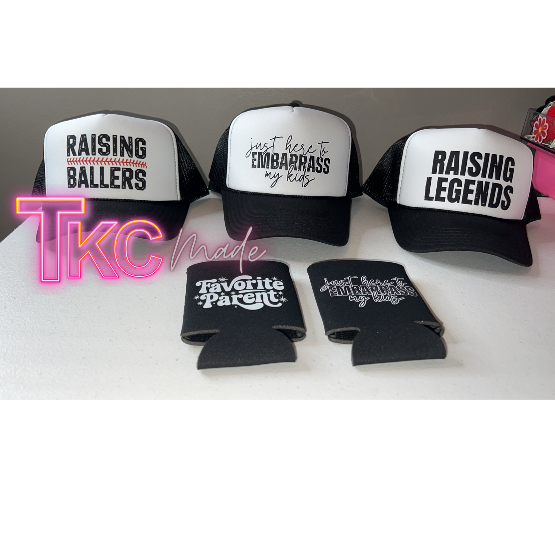 Three caps with humorous text and two can coolers on a white surface, branded with 'TKC Made'.