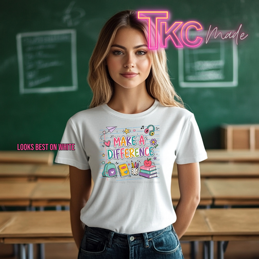 A woman stands in a classroom wearing a white graphic T-shirt with the phrase 'MAKE A DIFFERENCE' and colorful school-themed illustrations. The image includes a pink 'TKC made' logo at the top and 'LOOKS BEST ON WHITIE' text on the left.