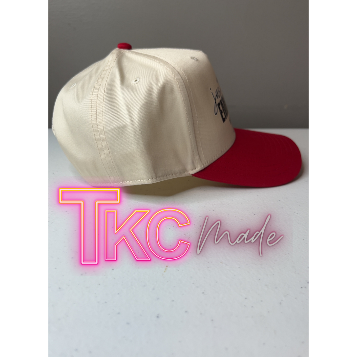 Beige and red cap on a light gray surface with 'TKC made' text in neon pink and white.