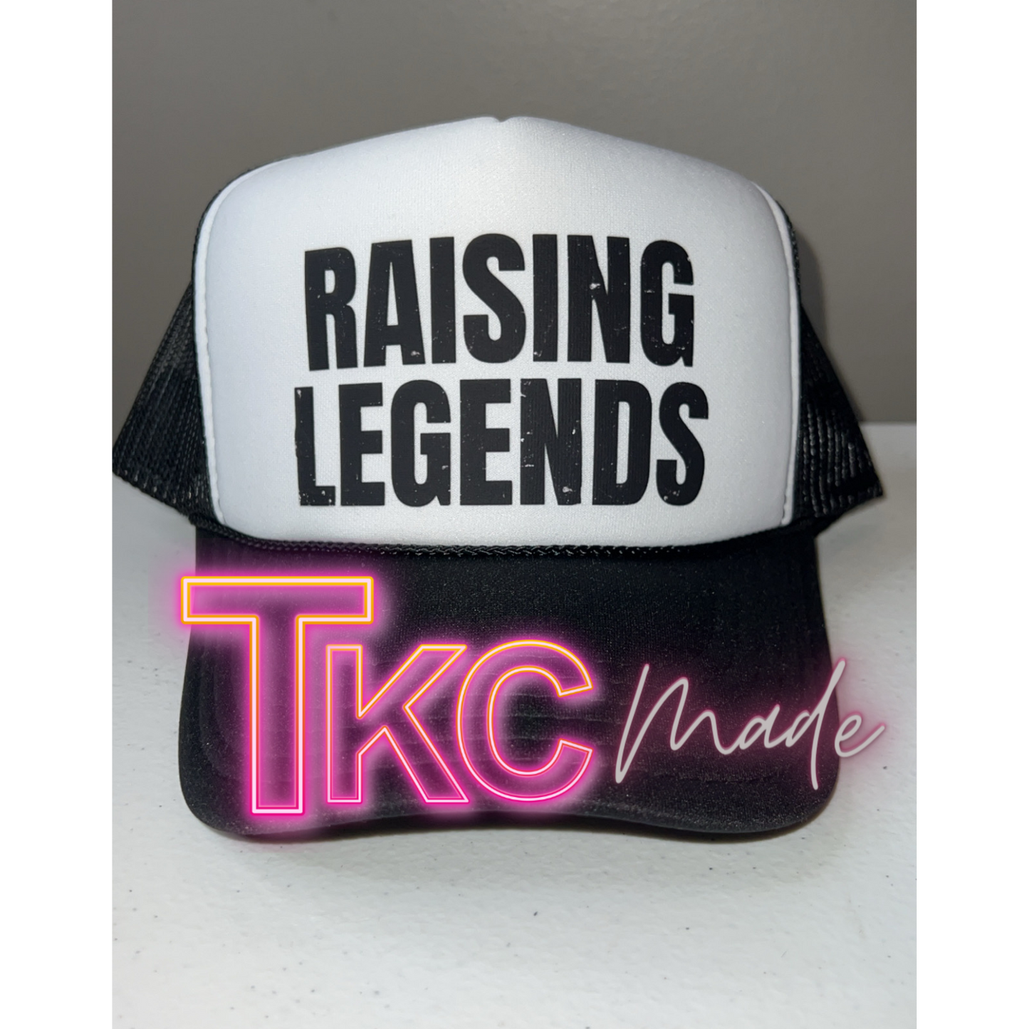 Trucker hat with 'RAISING LEGENDS' text and neon 'TKC made' design on a white background