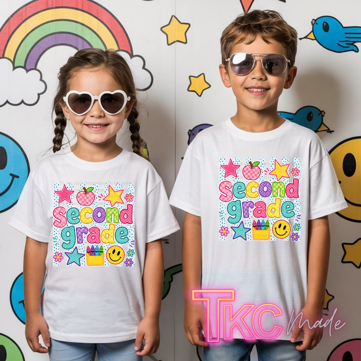 Two children wearing matching white graphic T-shirts that say 'Second Grade' in colorful letters, standing in front of a cartoon wall. The girl wears heart-shaped sunglasses, and the boy wears aviator sunglasses.