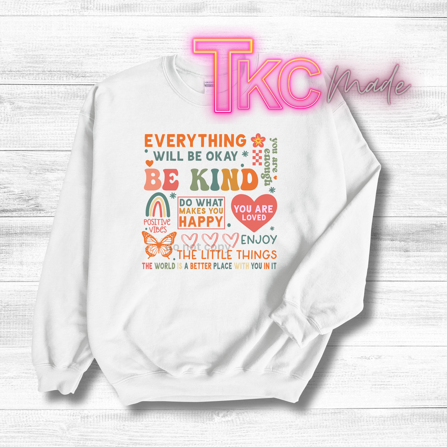 White sweatshirt with motivational quote on a white wooden background, featuring 'TKC made' branding.
