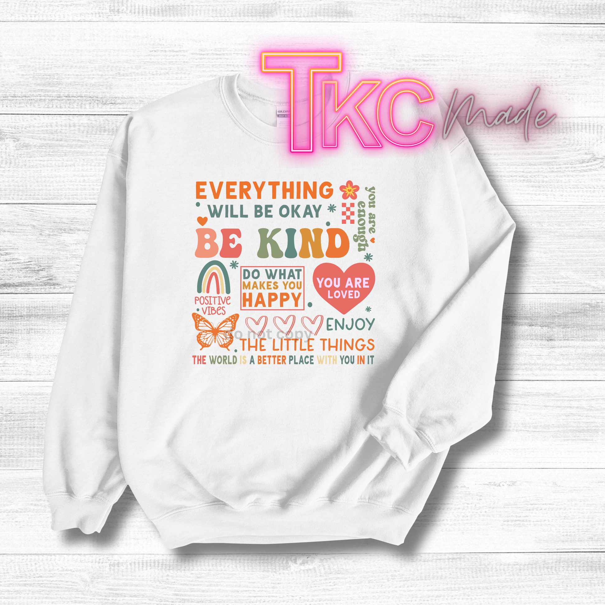 White sweatshirt with motivational quote on a white wooden background, featuring 'TKC made' branding.