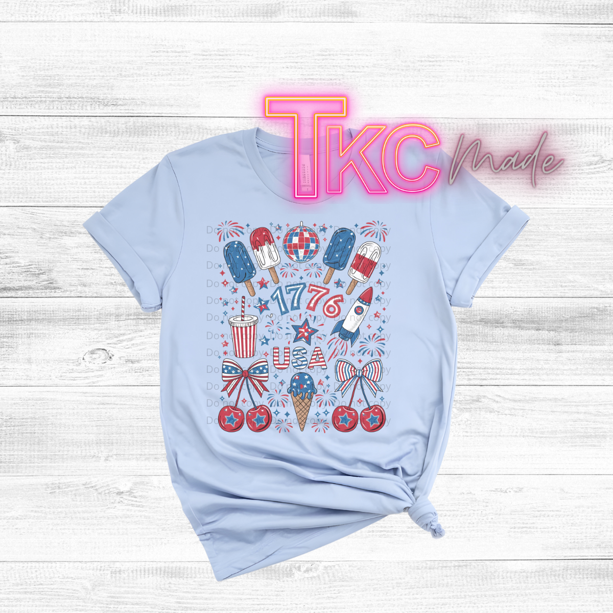 Light blue t-shirt with colorful graphics and 'TKC Made' branding on a wooden surface