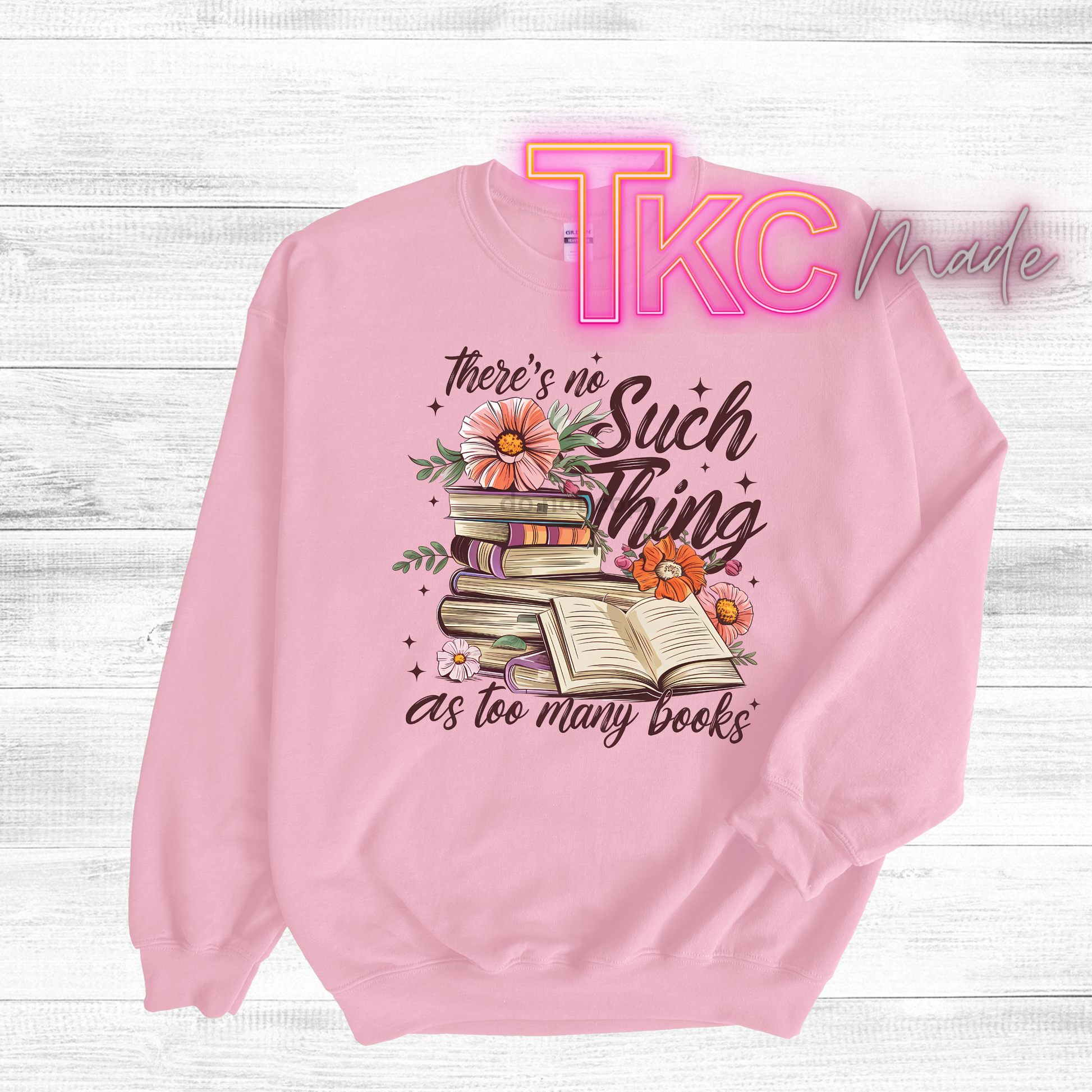 Pink sweatshirt with book-themed design and 'TKC Made' branding on a light wooden background