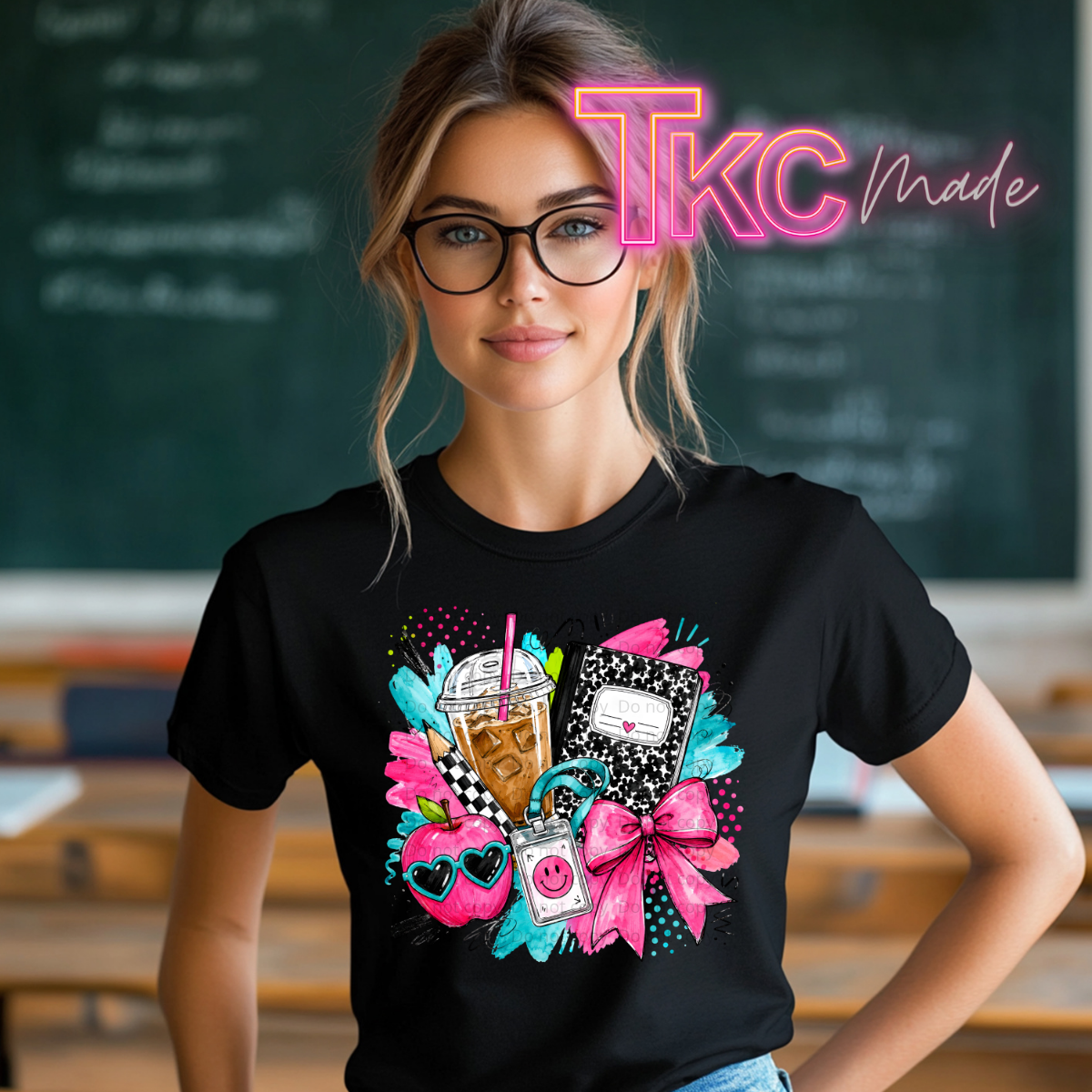 A woman wearing a black graphic t-shirt with a colorful design of a drink, heart sunglasses, and a pink bow, standing in front of a chalkboard. A neon-style 'TKC made' watermark is visible at the top.