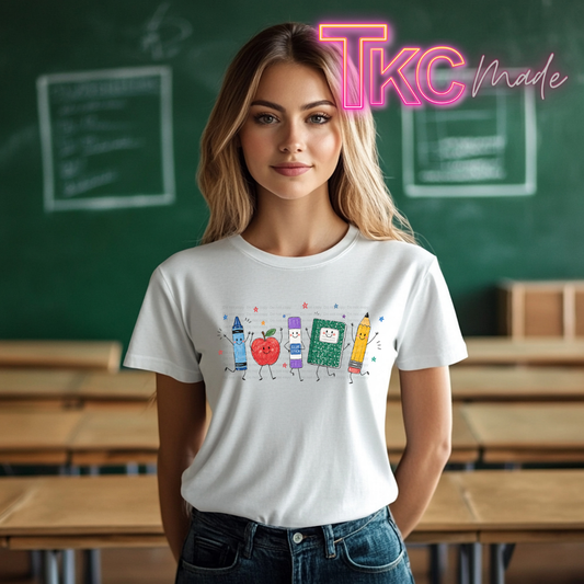 A woman wearing a white graphic T-shirt with a colorful cartoon crayon and apple design, standing in front of a green chalkboard classroom background. A pink 'Tkc Made' watermark is visible in the top right.