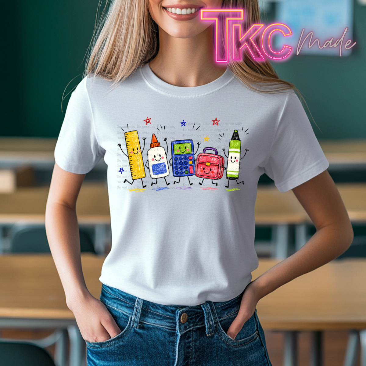 A woman wearing a white graphic t-shirt with a colorful cartoon illustration of school supplies (pencil, glue stick, calculator, backpack, marker) on the chest, set against a blurred classroom background. A 'TKC Made' watermark is visible in the top right corner.