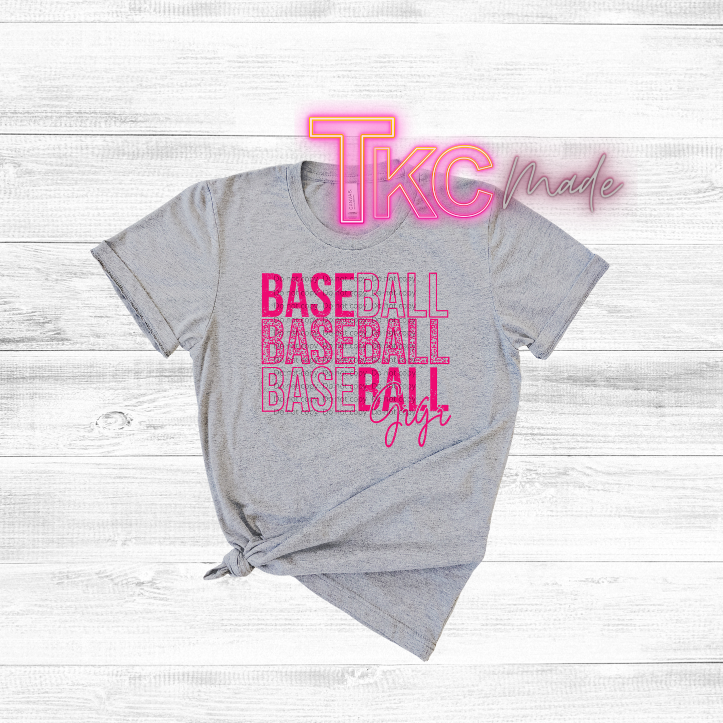 Gray t-shirt with pink 'TKC made' and 'BASEBALL BASEBALL BASEBALL GIRL' text on a light wooden background