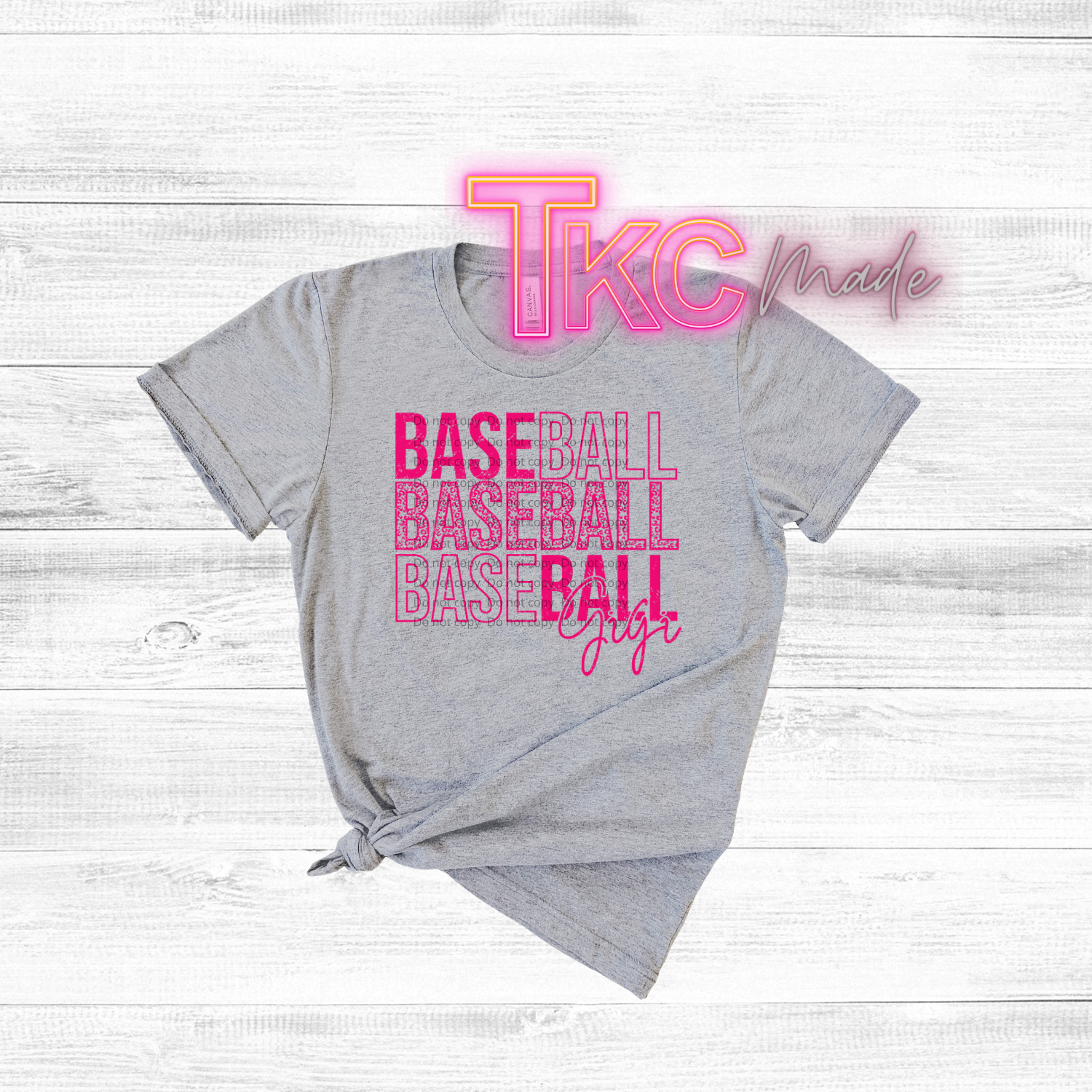 Gray t-shirt with pink 'TKC made' and 'BASEBALL BASEBALL BASEBALL GIRL' text on a light wooden background