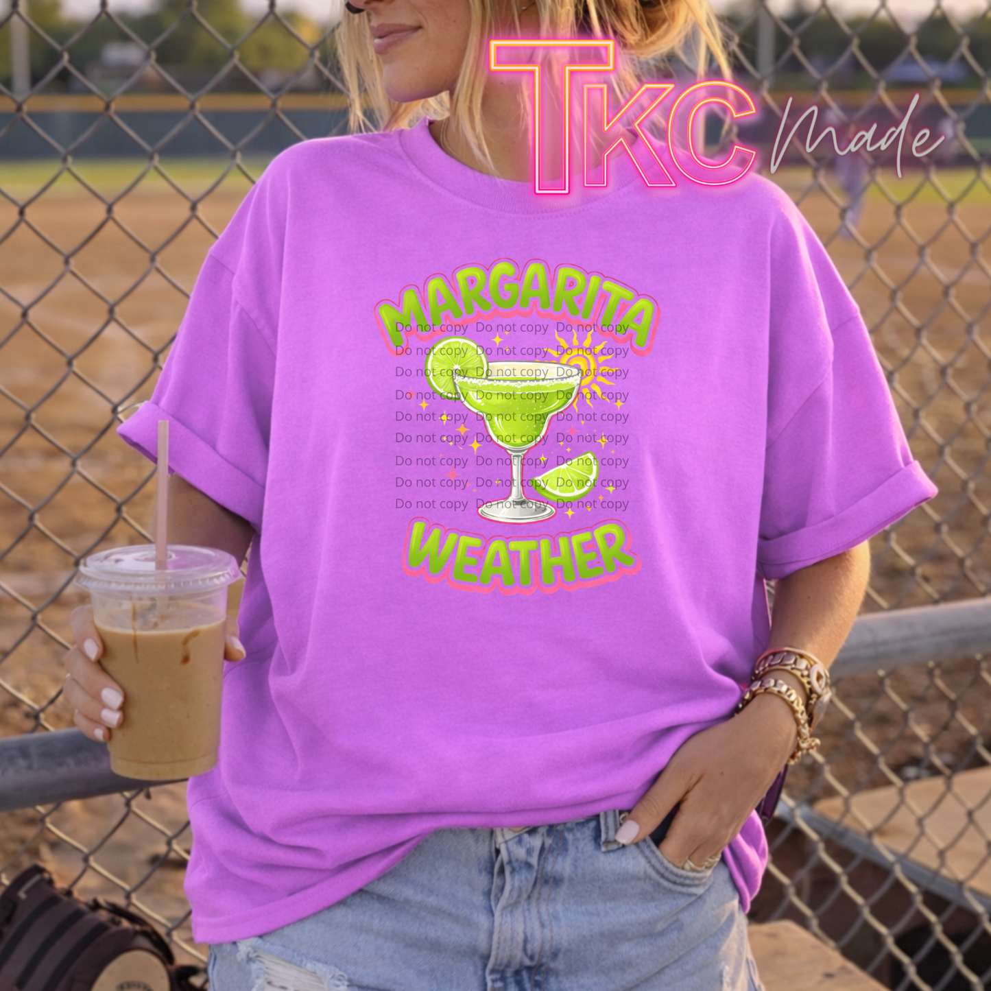 Person wearing a purple t-shirt with a margarita graphic and text, holding a drink.