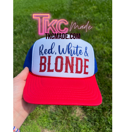 Trucker hat with 'Red, White & Blonde' text held in front of a grassy background