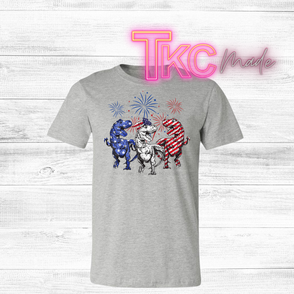 Gray t-shirt with cartoon dinosaurs in patriotic outfits and fireworks on a white background.