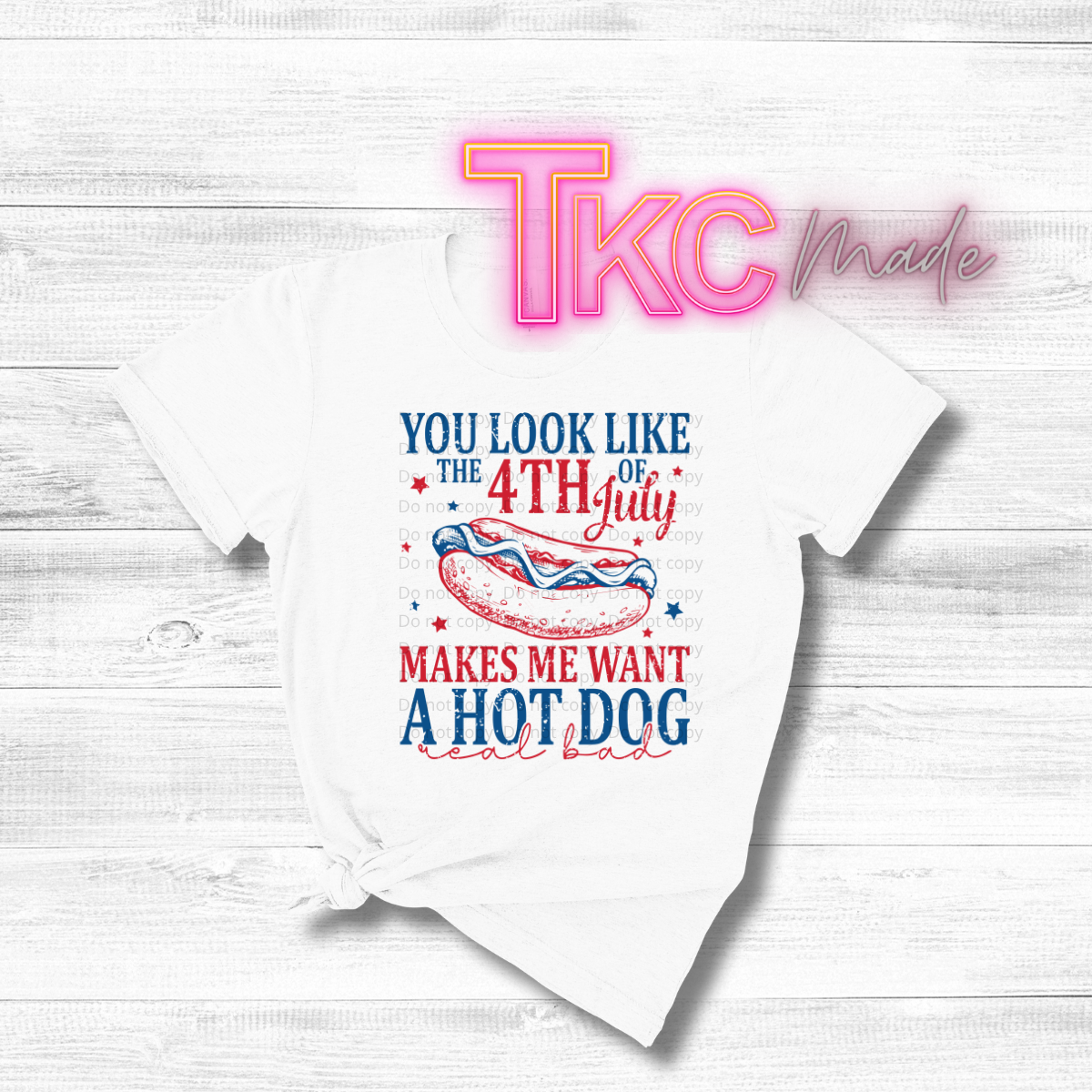 White t-shirt with 4th of July graphic and text on a wooden surface, featuring 'TKC Made' branding.