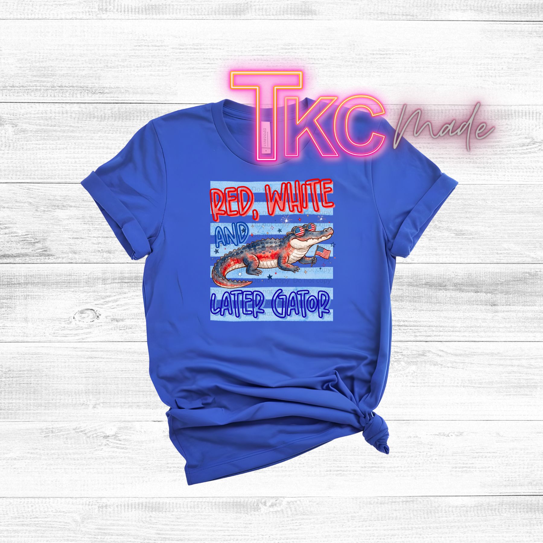 Blue t-shirt with a patriotic red white and gator graphic design and text on a wooden surface.