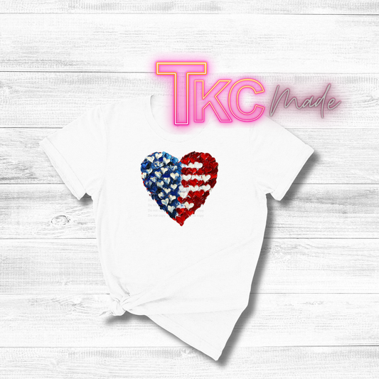 White baby onesie with a heart design on a wooden surface, featuring 'TKC Made' branding.