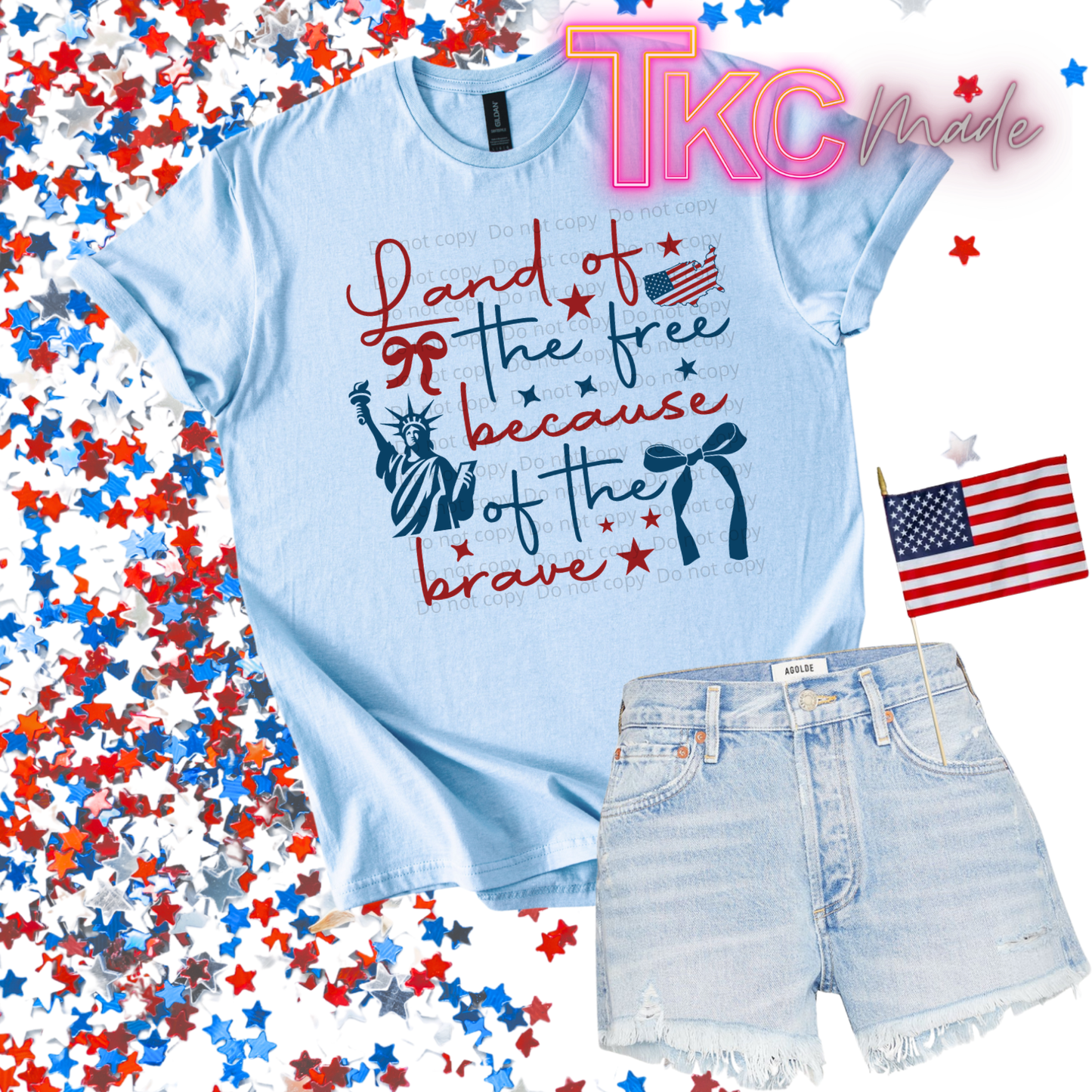 Light blue t-shirt with patriotic design that reads land of the free because of the brave and denim shorts on a background with American flags and confetti.