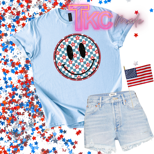 Light blue t-shirt with happy face design and denim shorts on a background with red, white, and blue stars and an American flag.