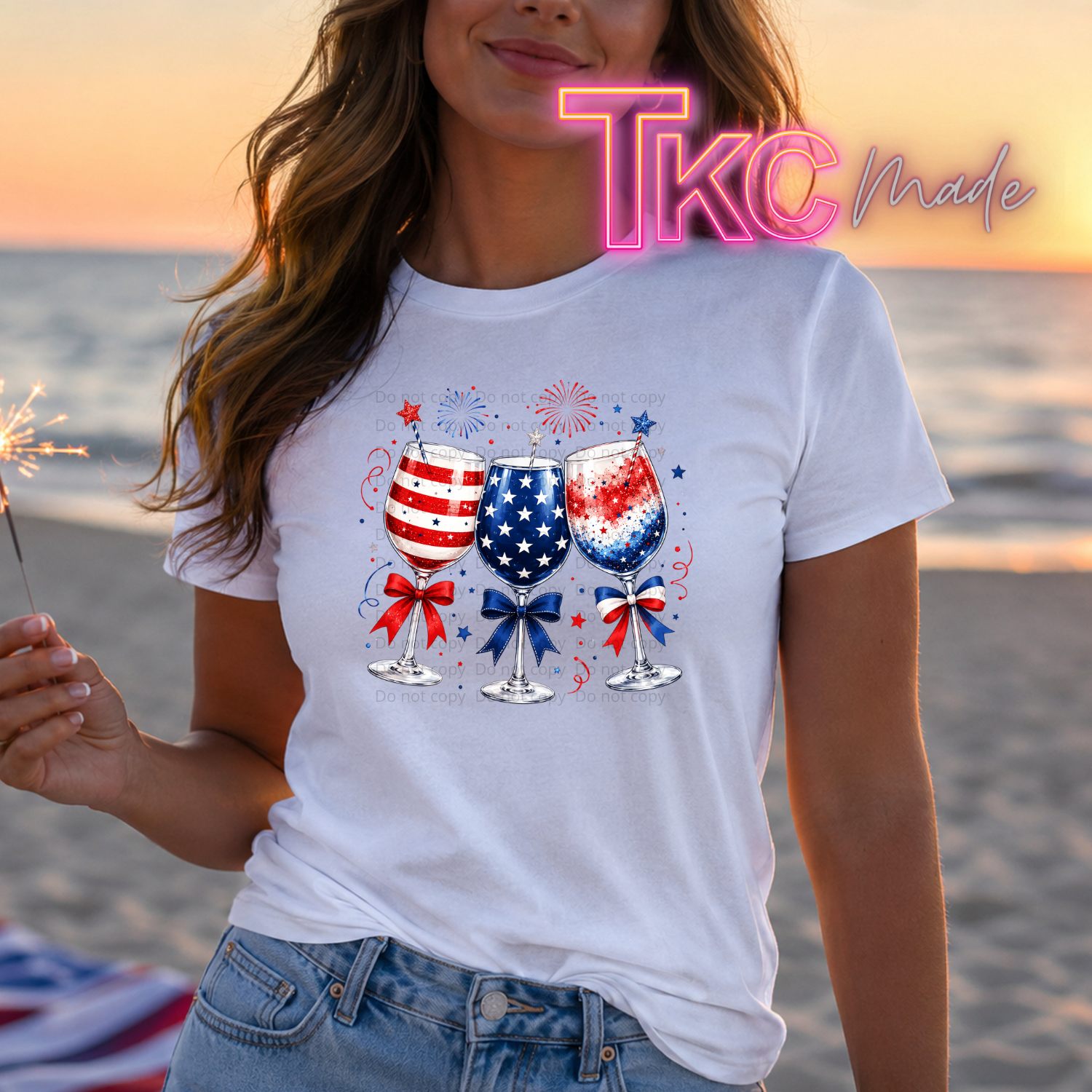Person wearing a white t-shirt with colorful glass designs on a beach at sunset.