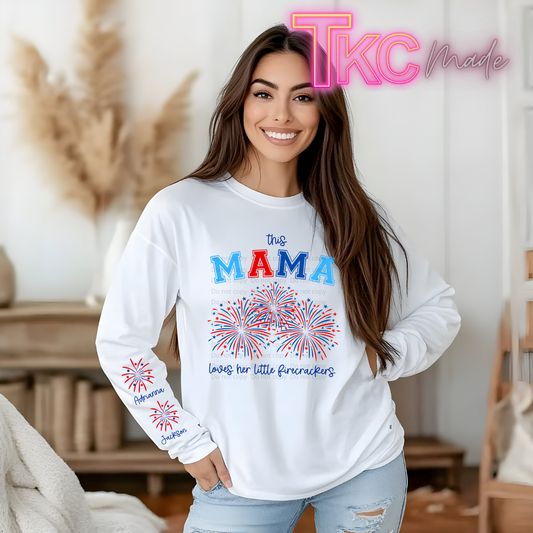 Woman wearing a white sweatshirt with 'this MAMA loves her little firecrackers' text and fireworks design, indoors.