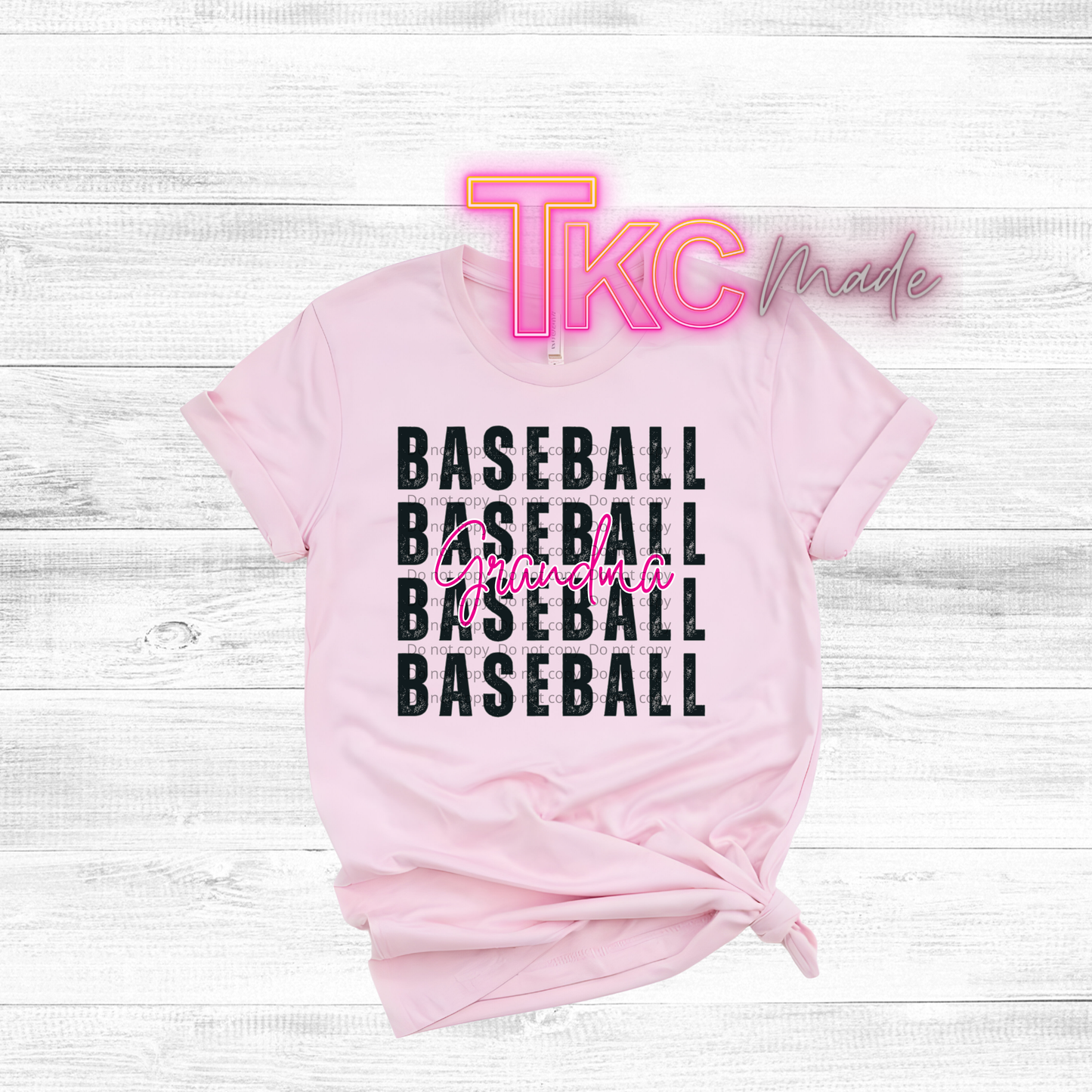 Pink t-shirt with 'Baseball Grandma' text and 'TKC made' branding on a white wooden surface