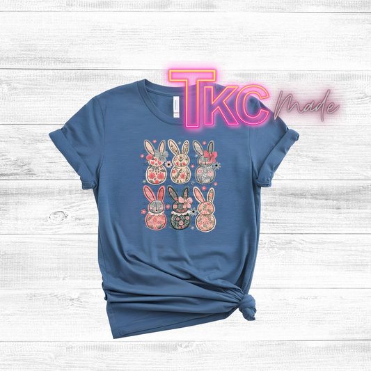 Blue t-shirt with floral bunny design on a white wooden background, featuring 'TKC made' text.