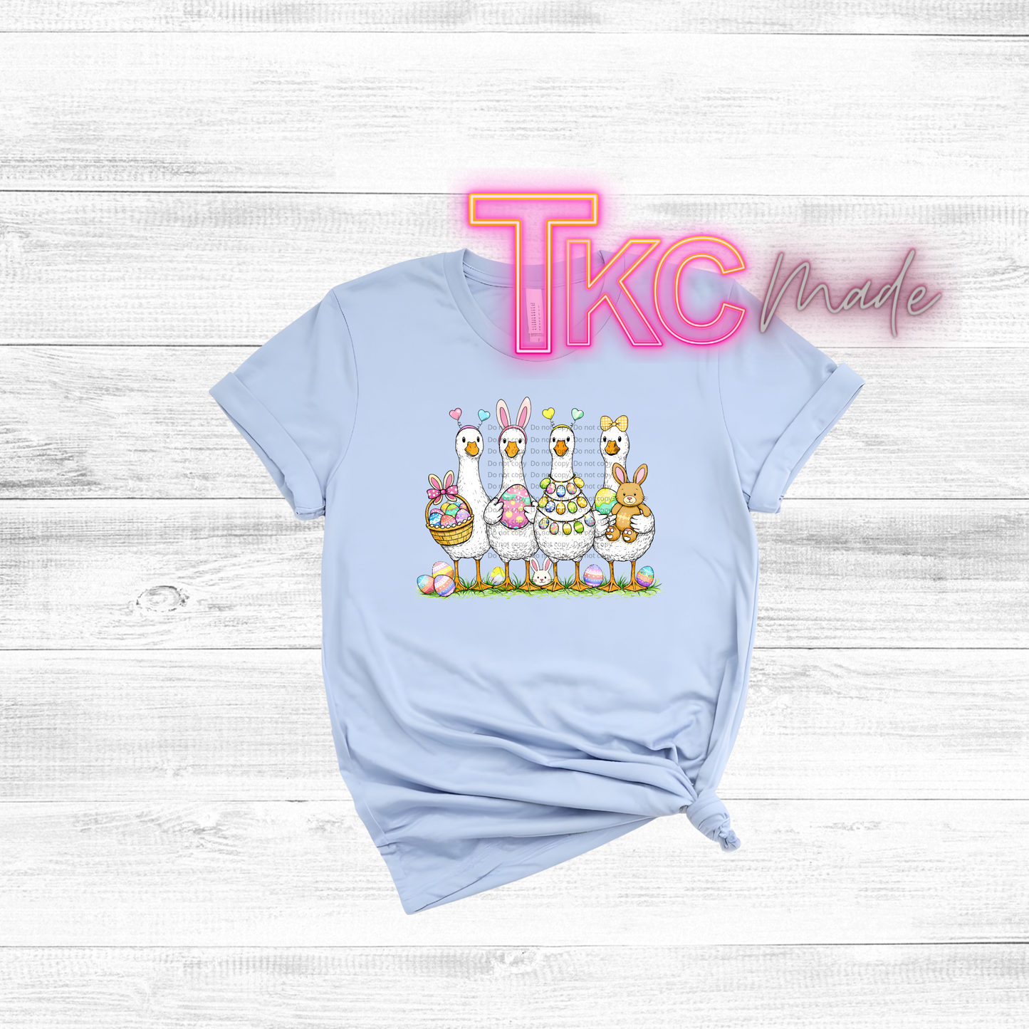Light blue t-shirt with cartoon goose and Easter eggs on a white wooden background, featuring 'TKC Made' text.