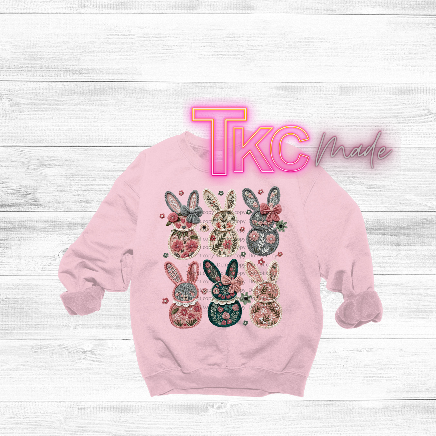 Pink sweatshirt with floral bunny designs on a white wooden background, featuring 'TKC Made' text.