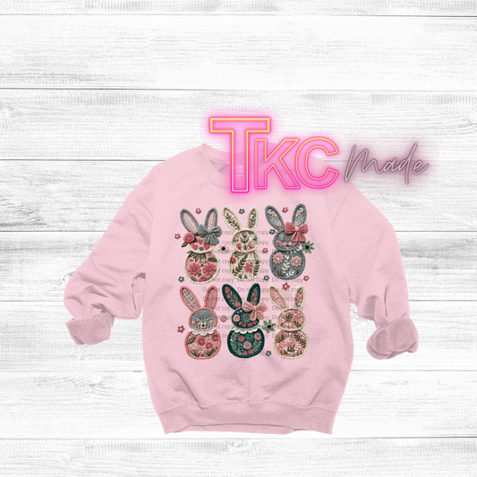 Pink sweatshirt with floral bunny designs on a white wooden background, featuring 'TKC Made' text.