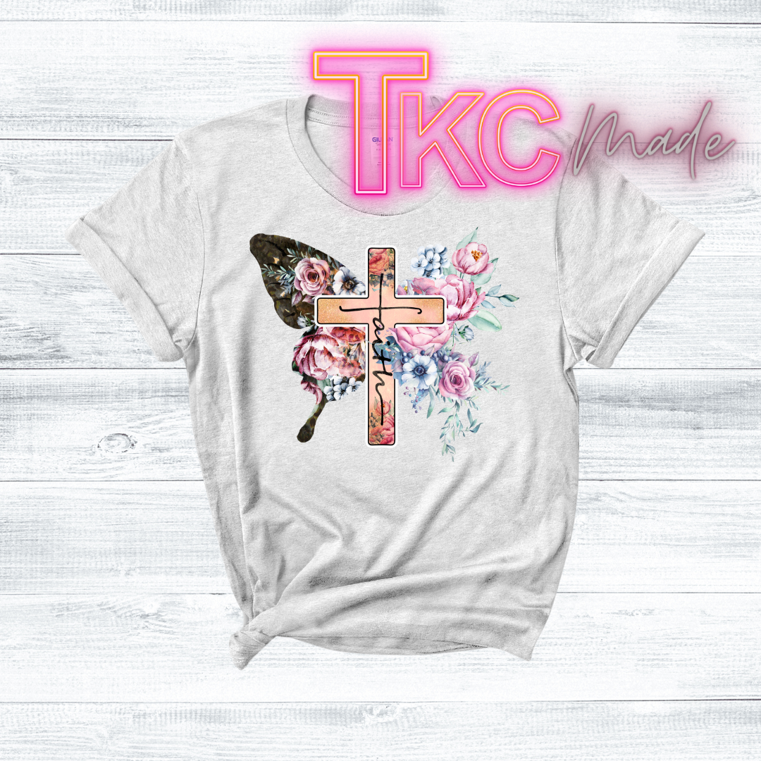 White t-shirt with floral cross design on a light wooden background, featuring 'TKC Made' text.