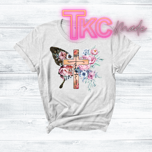 White t-shirt with floral cross design on a light wooden background, featuring 'TKC Made' text.