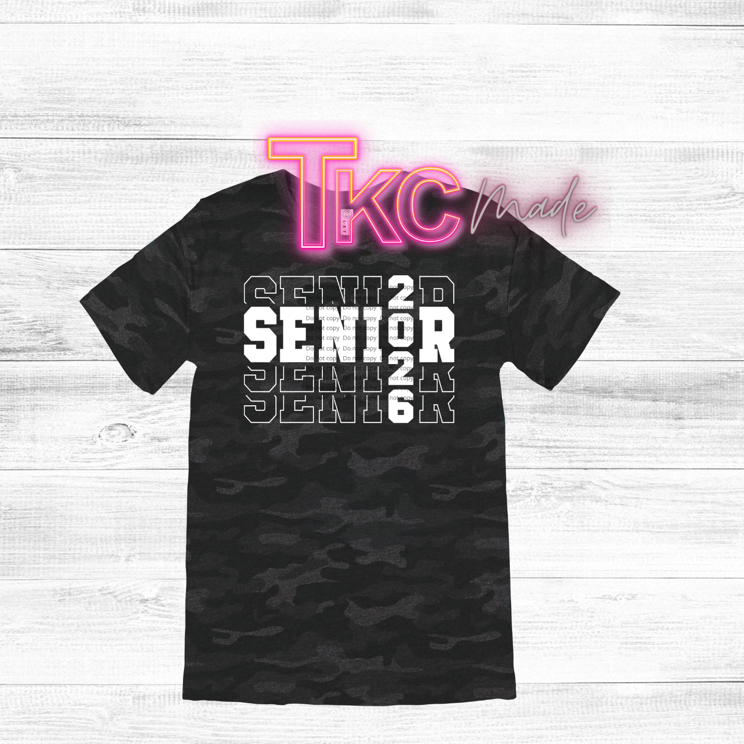 Black camouflage t-shirt with 'SENIOR 2026' text and 'TKC Made' branding on a white wooden background