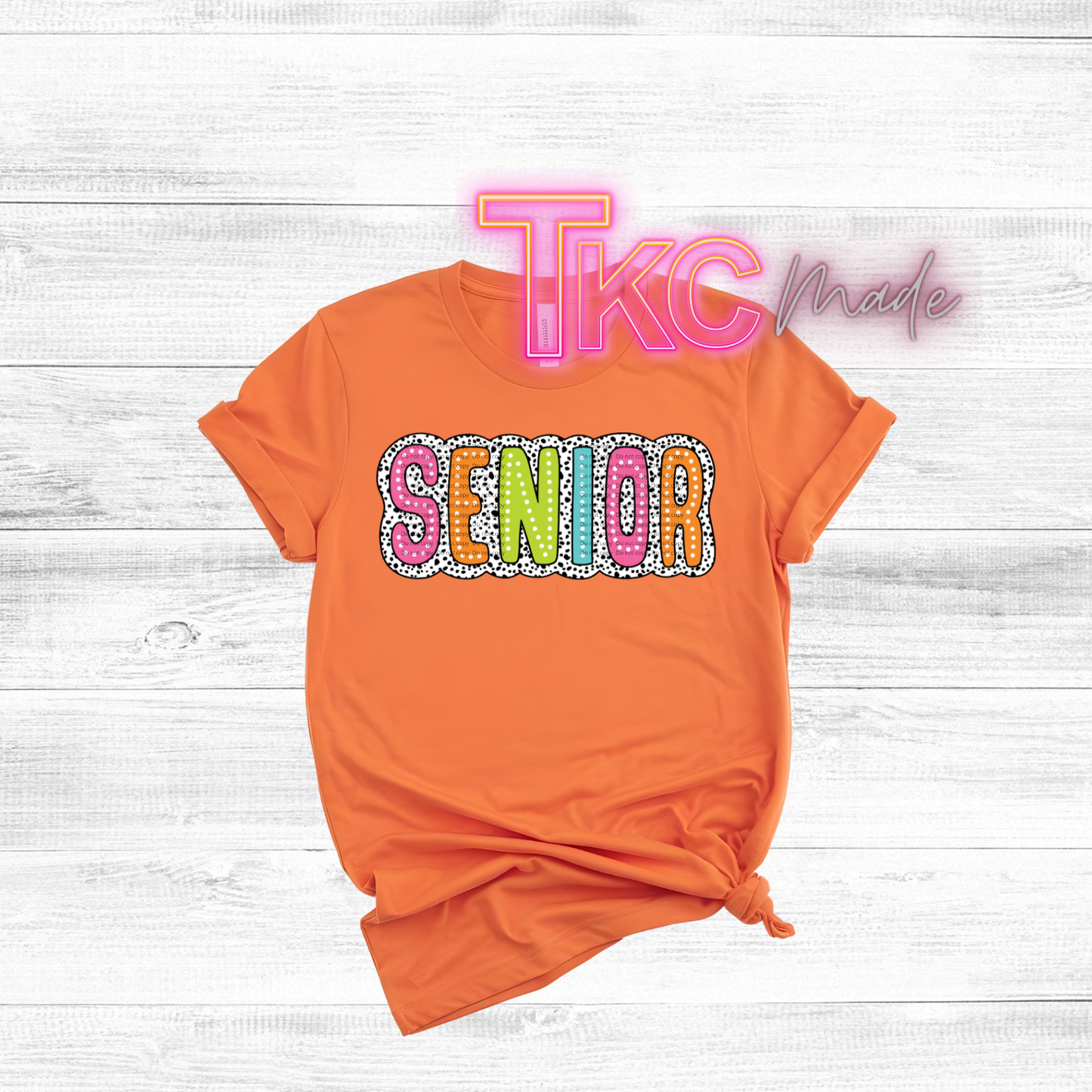 Orange t-shirt with colorful 'SENIOR' text on a white wooden surface, featuring 'Tikc Made' branding.
