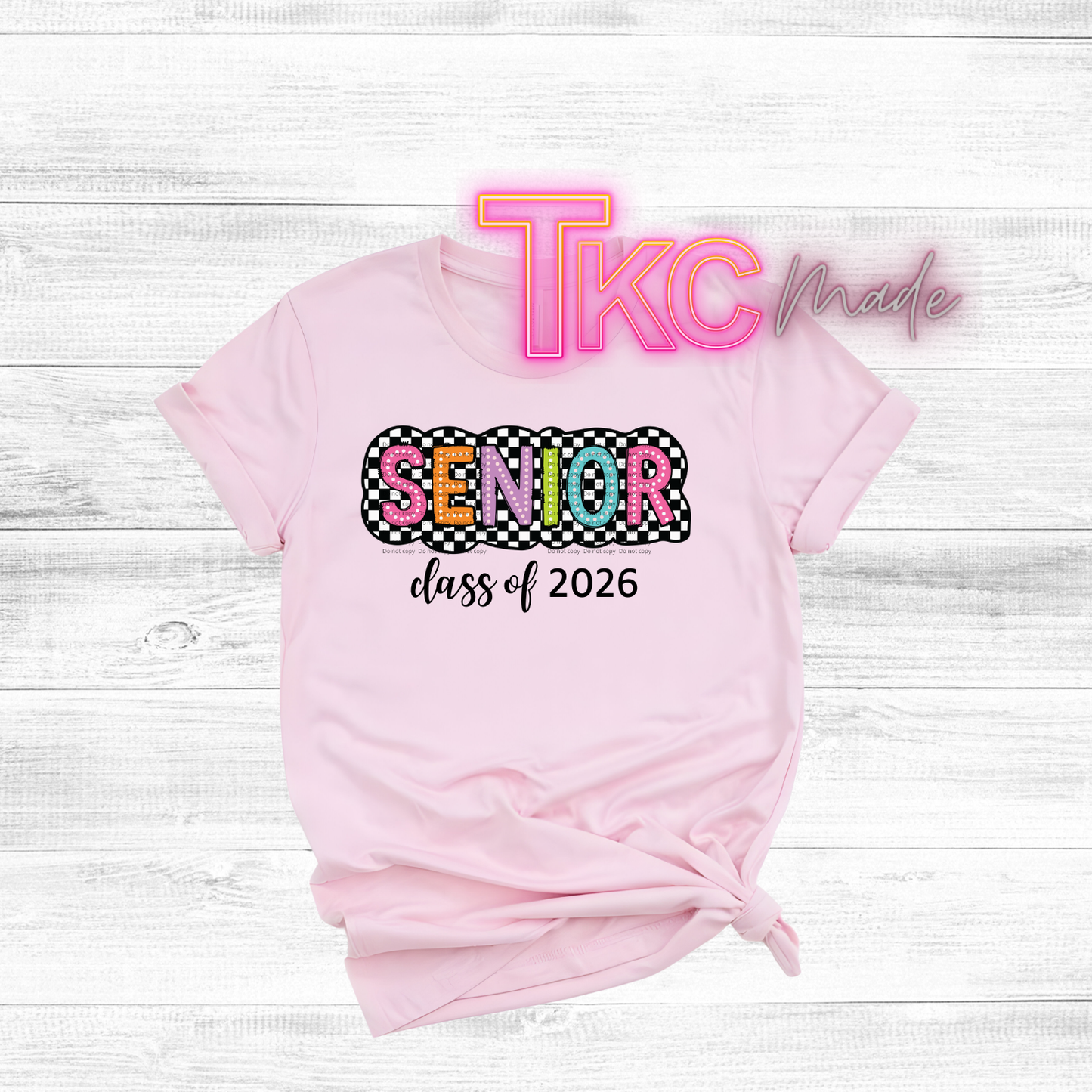 Pink t-shirt with 'Senior class of 2026' text on a white wooden background