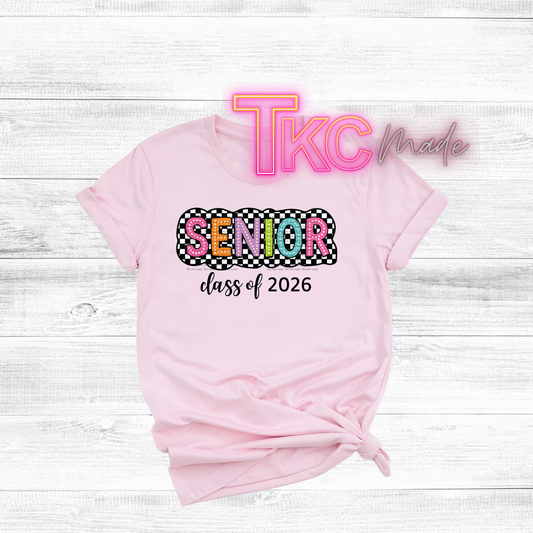 Pink t-shirt with 'Senior class of 2026' text on a white wooden background