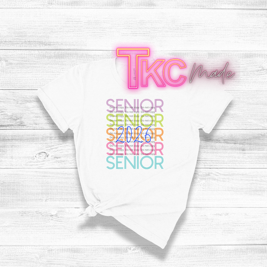White t-shirt with 'TKC made' and 'Senior 2026' text on a light wooden surface