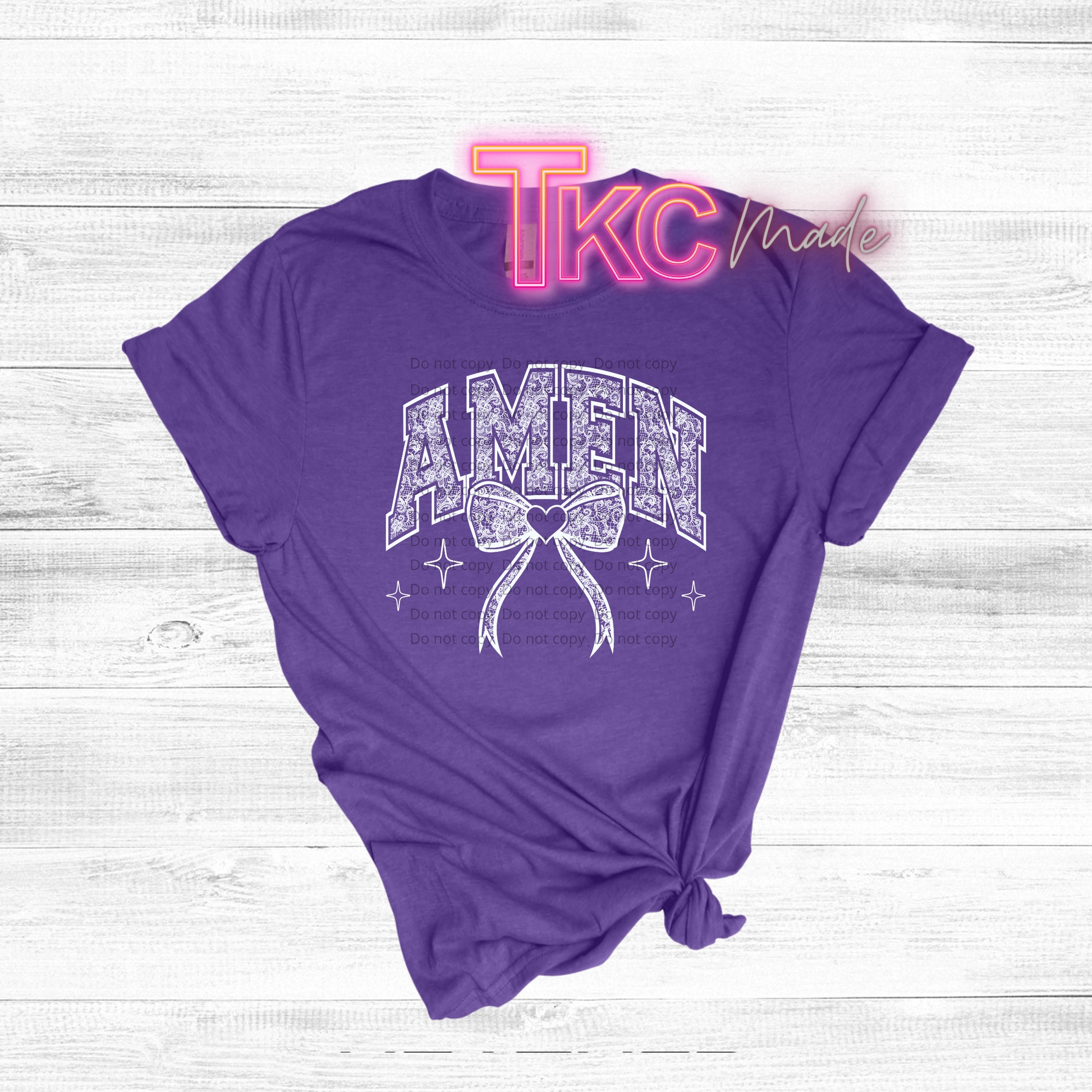 Purple t-shirt with 'AMEN' graphic on a light wooden surface, featuring 'TKC Made' branding.