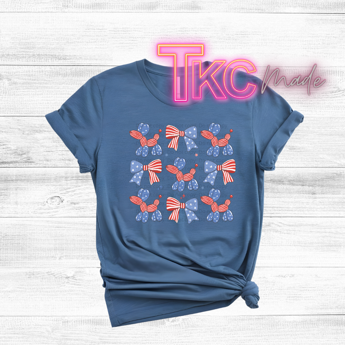 Blue t-shirt with red and white bow design on a wooden surface with 'TKC Made' text.