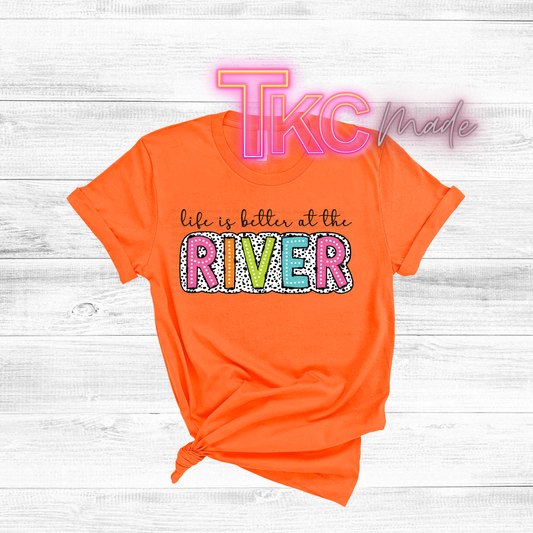 Orange t-shirt with colorful text 'life is better at the RIVER' on a light wooden background