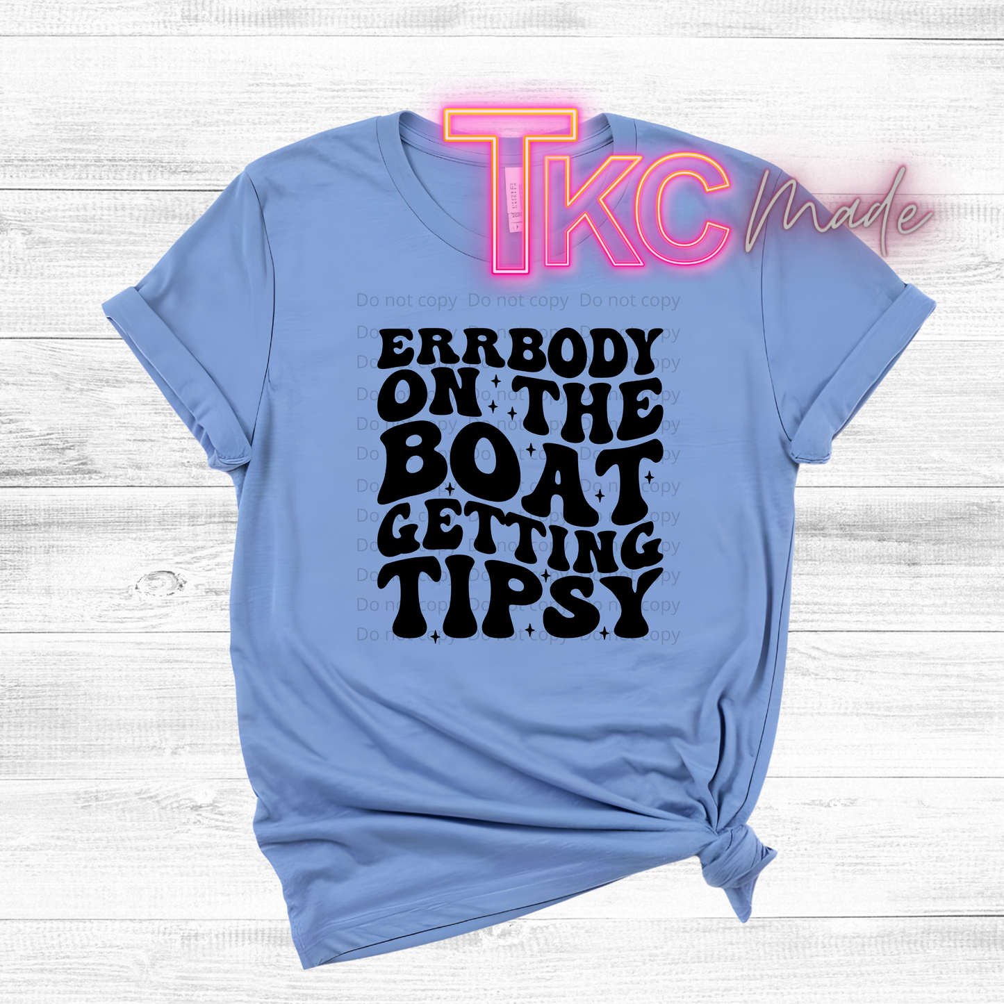 Light blue t-shirt with black text on a white wooden background, featuring 'TKC Made' logo.