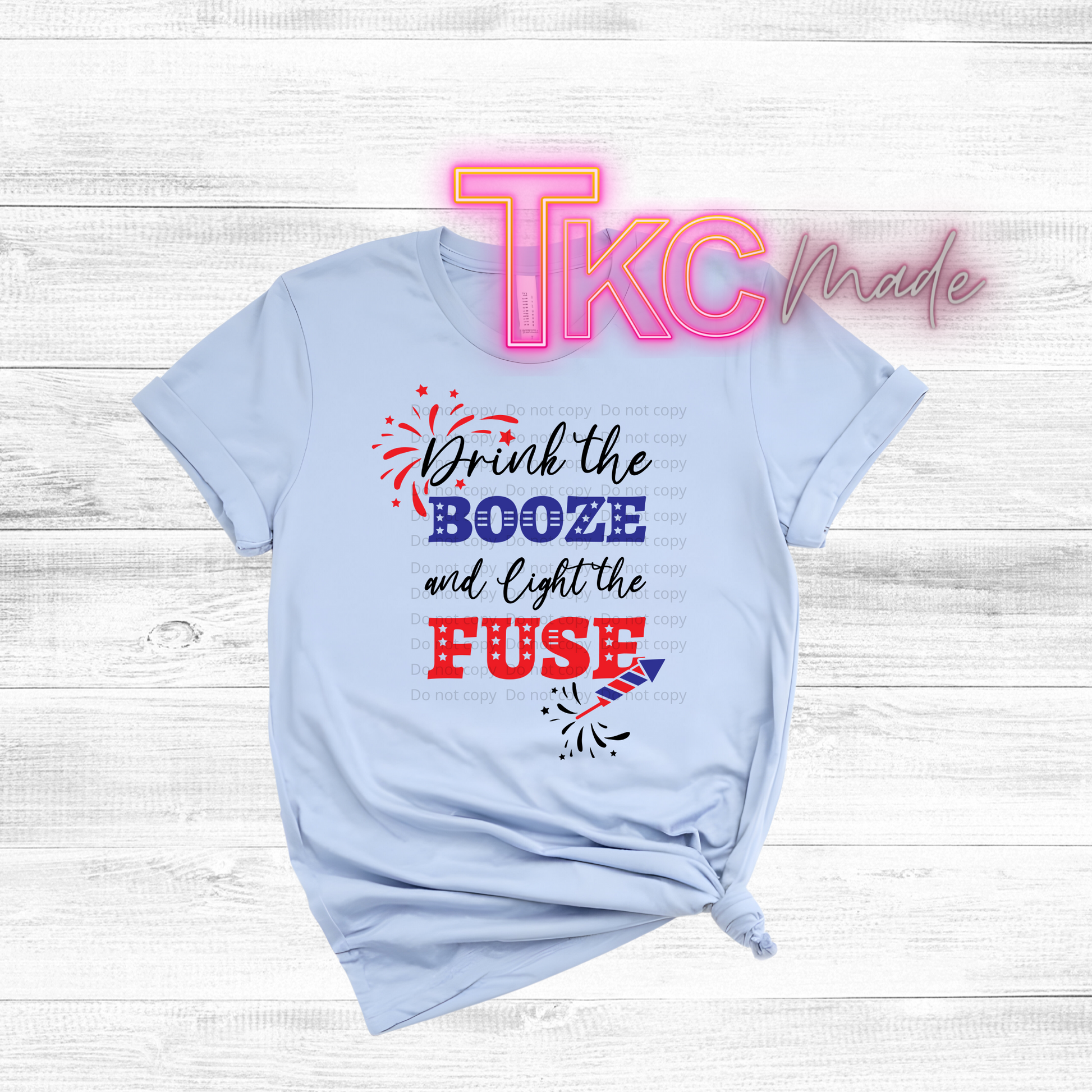 Light blue t-shirt with colorful text and graphics on a wooden surface with 'TKC Made' in the background.