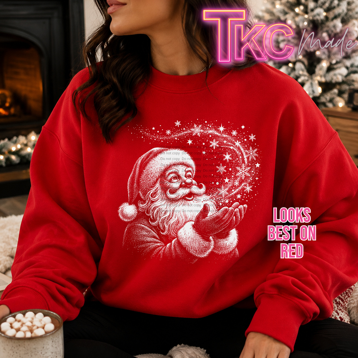 A woman wearing a bright red crewneck sweatshirt with a white glittery Santa Claus graphic blowing a snowflake heart. The image has a 'TKC made' watermark in the top right and 'LOOKS BEST ON RED' text on the right side.