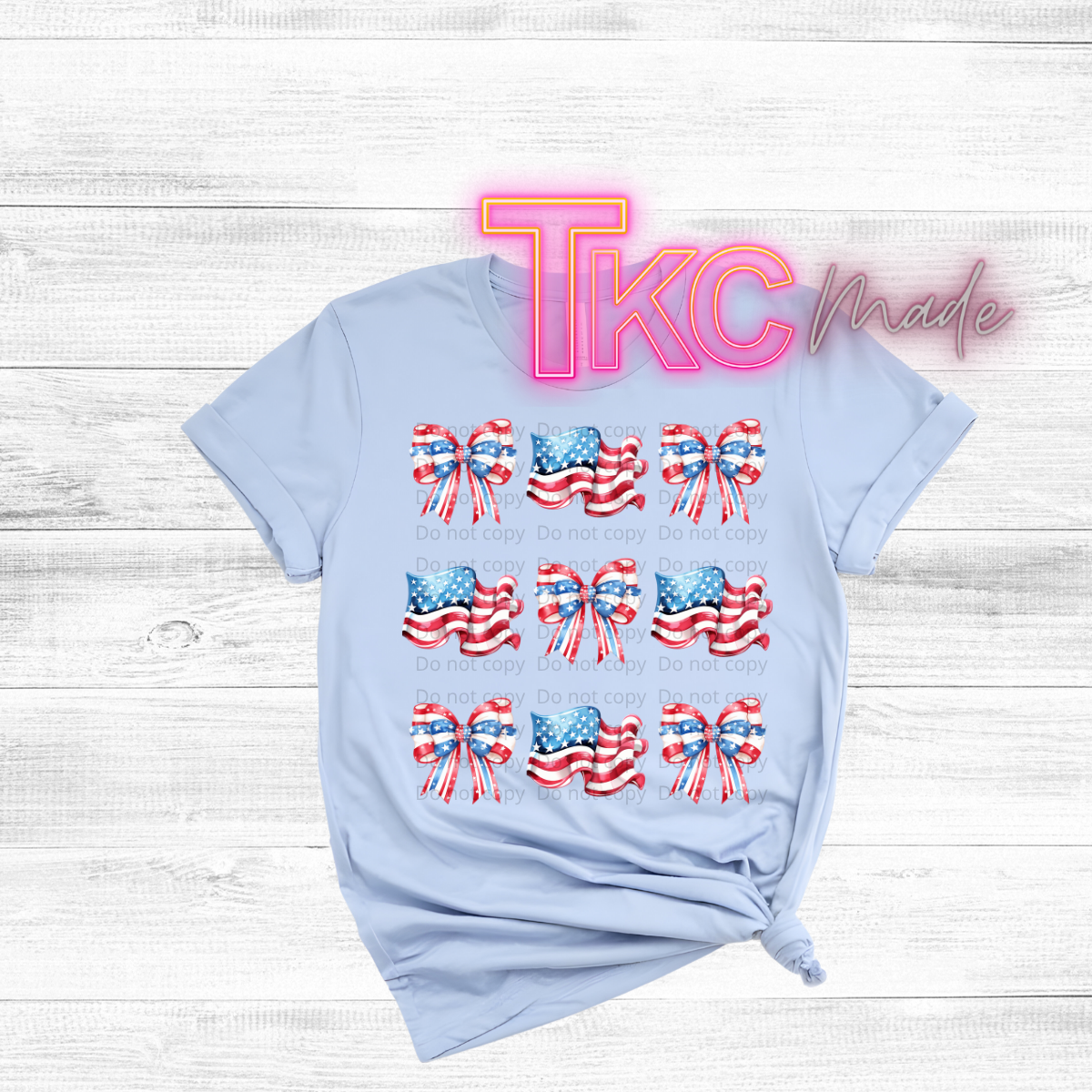 Light blue t-shirt with American flag designs and 'TKC made' text on a wooden surface