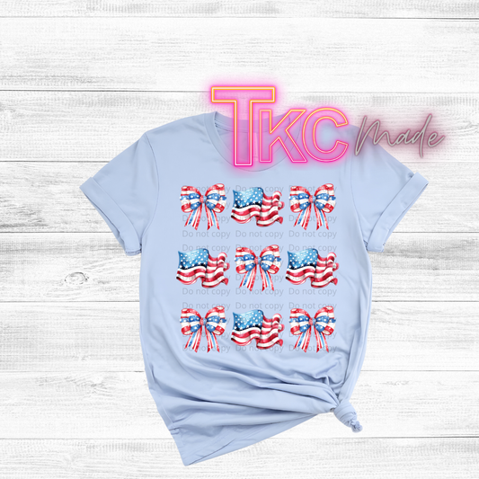 Light blue t-shirt with American flag designs and 'TKC made' text on a wooden surface