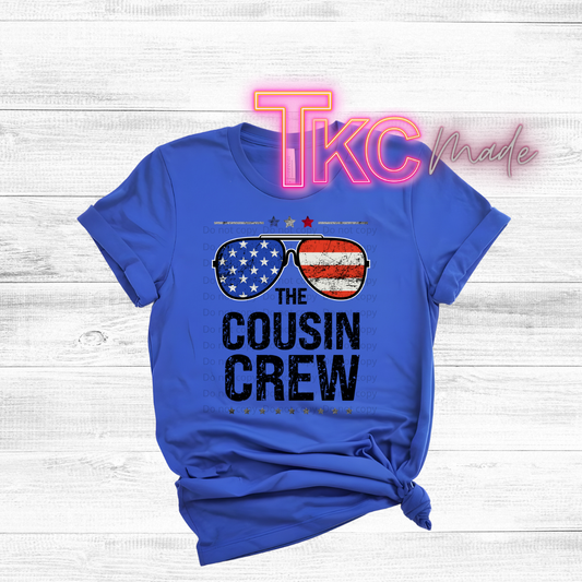 Blue t-shirt with 'The Cousin Crew' design on a wooden surface, featuring the brand 'TKC Made'.