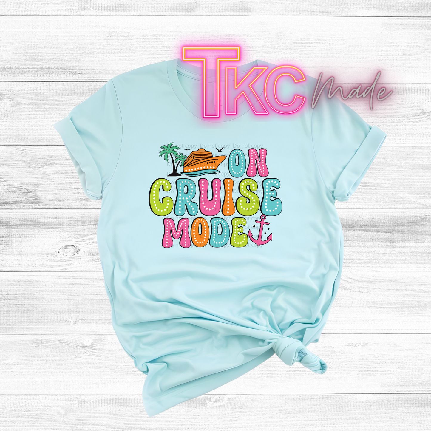 Light blue t-shirt with colorful 'On Cruise Mode' text and palm tree design on a white wooden background.
