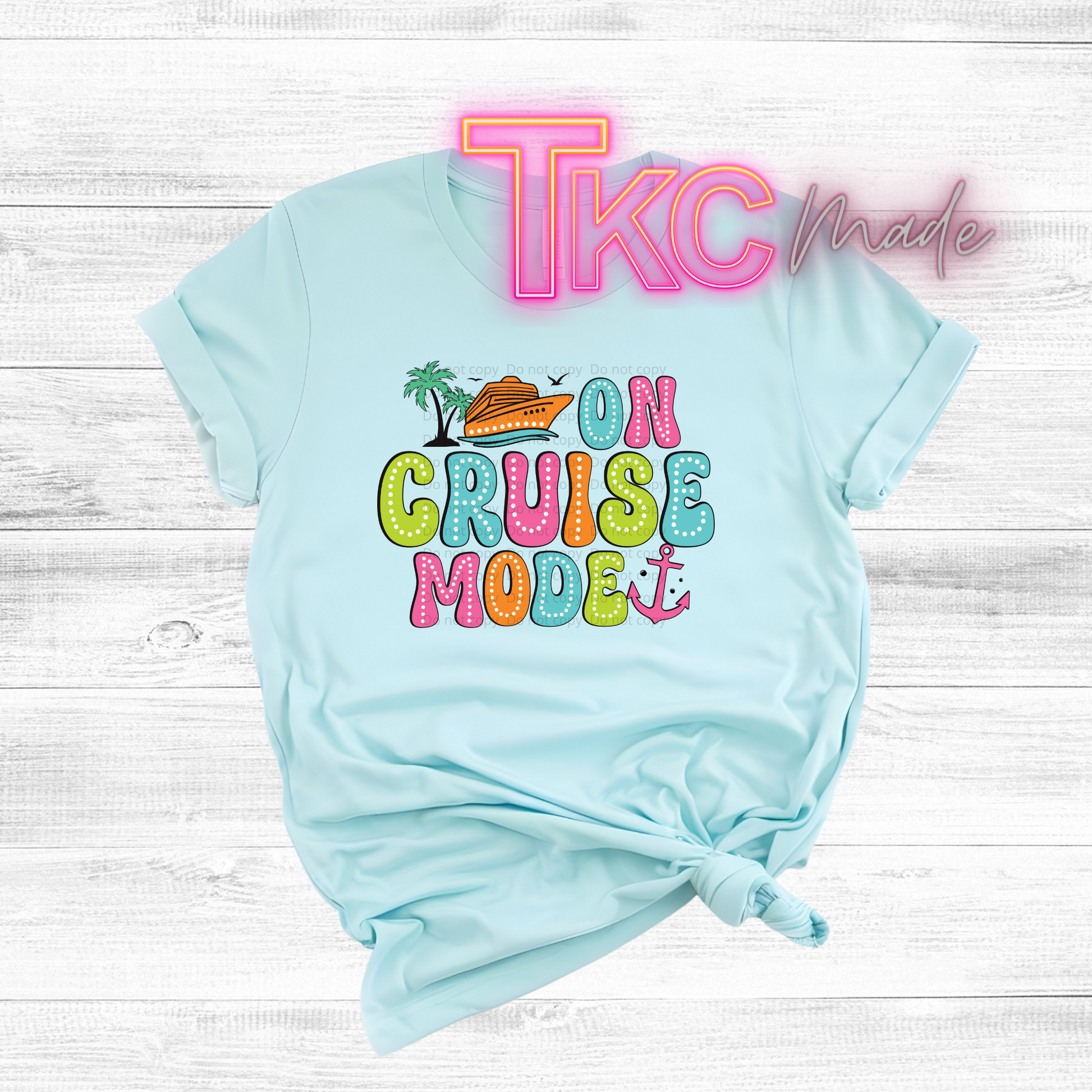 Light blue t-shirt with colorful 'On Cruise Mode' text and palm tree design on a white wooden background.