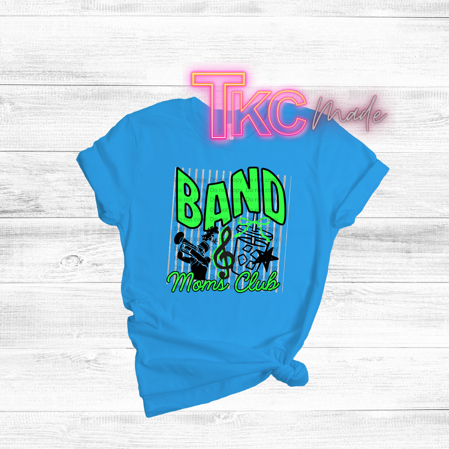 Blue t-shirt with 'Band Moms Club' design and 'TKC made' text on a light wooden background