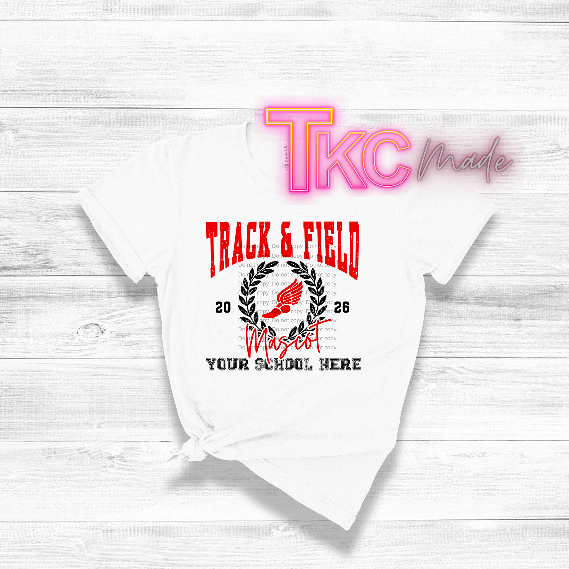 White t-shirt with 'Track & Field' design and 'TKC Made' branding on a light wooden surface.
