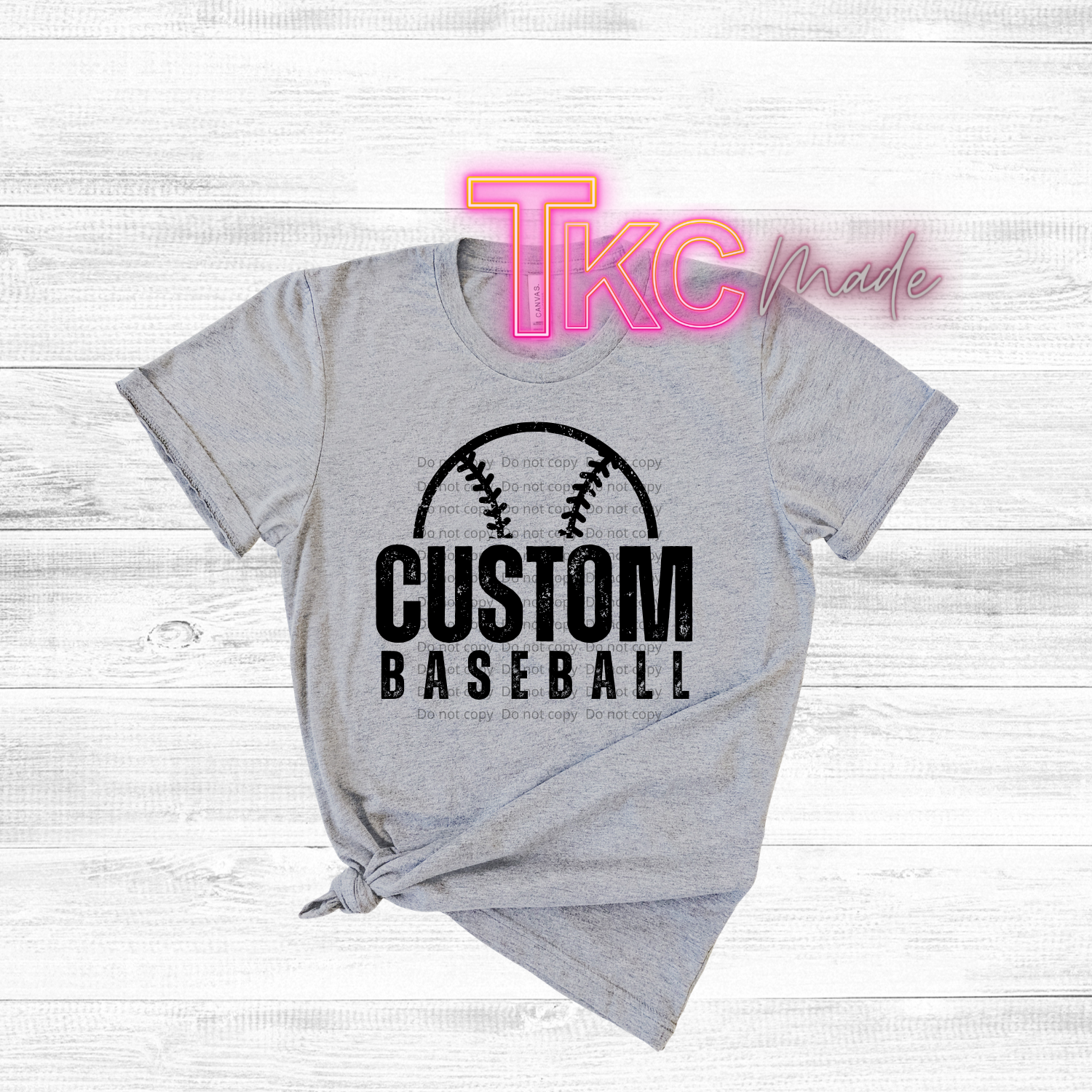 Gray t-shirt with 'Custom Baseball' design on a wooden surface, featuring the brand 'TKC made'.
